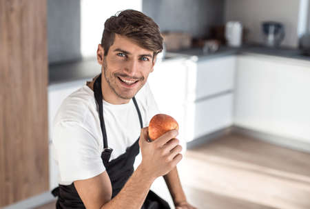 attractive man with an apple sitting in a home kitchenの写真素材