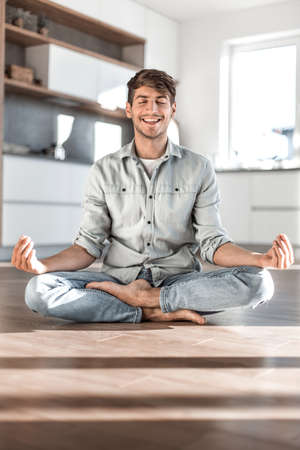 young man sitting in Lotus position on kitchen floorの写真素材