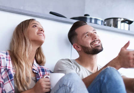 young couple drinking coffee sitting on the kitchen floor