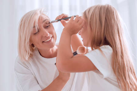 Mother and young daughter playing and applying make up togetherの写真素材