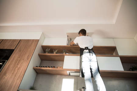 young man standing near a high kitchen shelf