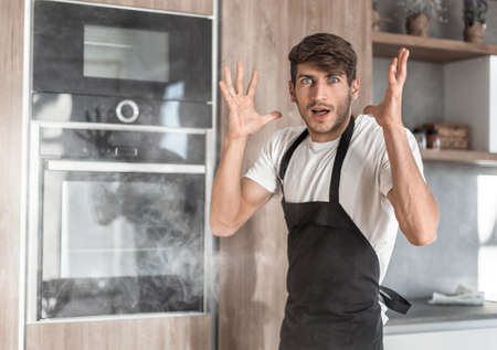 surprised young man standing near broken ovenの写真素材