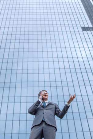 happy business man with smartphone standing in front of high rise office building. photo with copy spaceの写真素材