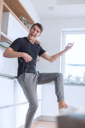 happy young man with smartphone sings in his kitchen