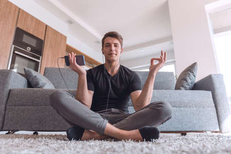 casual guy sitting in Lotus position on carpet in his living roomの写真素材