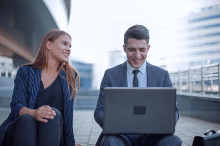 young business couple use laptop sitting near office buildingの写真素材