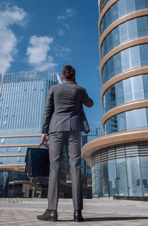 rear view. businessman with smartphone looking at tall office building. photo with copy spaceの写真素材