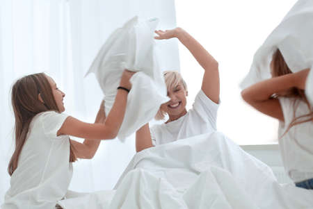 children are having a pillow fight on her mothers bed.の写真素材