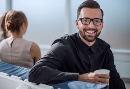 young businessman with a Cup of coffee sitting in a modern office.の写真素材