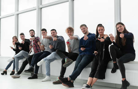 smiling young people with smartphones sitting near an office window.