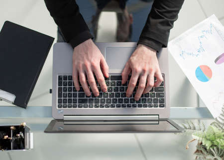 Man working by using a laptop computer on wooden table. Hands typing on a keyboard.