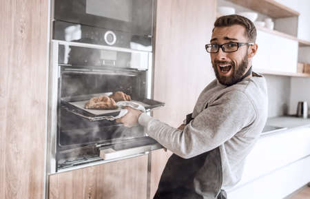 close up. a young man takes out of the oven tray of croissantsの写真素材