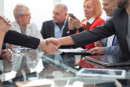 Business people shaking hands in modern office with colleagues meeting around table
