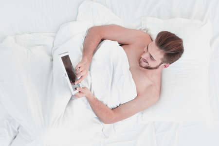smiling man using digital tablet lying on bedの写真素材