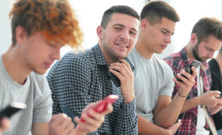 group of young people with smartphones sitting in one rowの写真素材