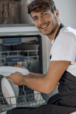 handsome young man sitting near an open dishwasherの写真素材