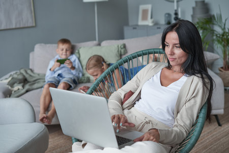 woman using laptop with interest at home while child relax on sofaの写真素材