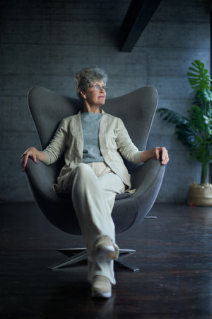 Sophisticated elegant beautiful 50s attractive middle aged smiling woman model sitting in chair looking at camera at homeの写真素材