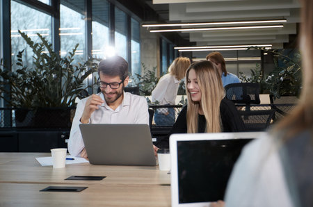 A group of people are working in a large office with many plants