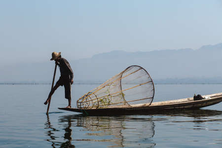 Inle Lake, Myanmar - FEB 25th 2014: Fisherman Rowing His Boat On Inle Lake In Myanmar At Sunset Using His Leg and with a conical fishing net on his boat.のeditorial素材