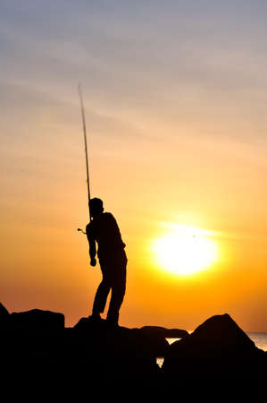 The silhouette of the guy with a fishing tackle, at sunset, which fishesの写真素材