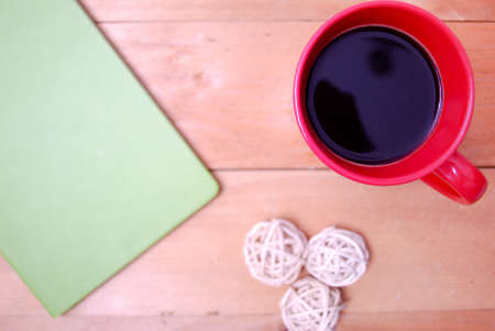 Wooden palette office desk table with coffee in red mug, rattan ball, green notebook and green...