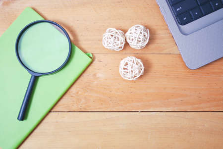 Wooden palette office desk table with laptop, rattan ball, green notebook and magnifying glass. Top...