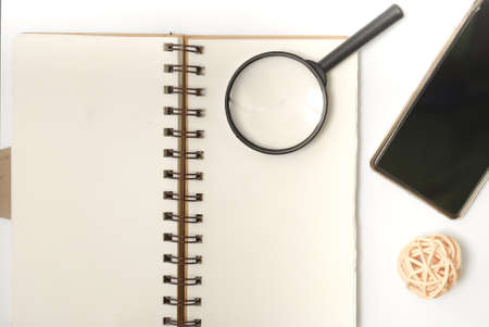 White office desk table with open note book, magnifying glass, rattan ball and smartphone. Top view with copy space, flat lay.の写真素材