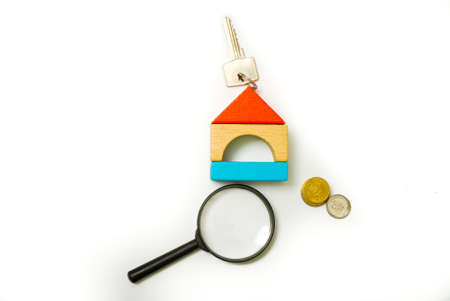 Conceptual image of miniature home icon made from wood bricks with key, coin and magnifying glass on isolated white backgroundの写真素材