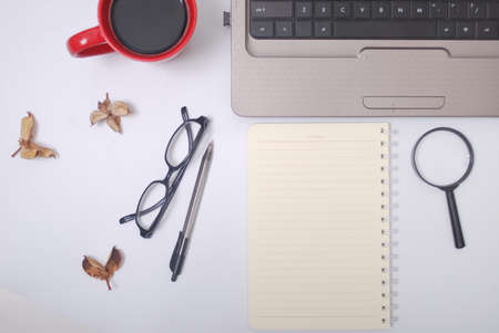 Stylish office table desk. Workspace with laptop, notebook, spectacle, pen, magnifying glass, cup of coffee on white background. Flat lay, top viewの写真素材