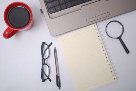 Stylish office table desk. Workspace with laptop, notebook, spectacle, pen, magnifying glass, cup of coffee on white background. Flat lay, top viewの写真素材