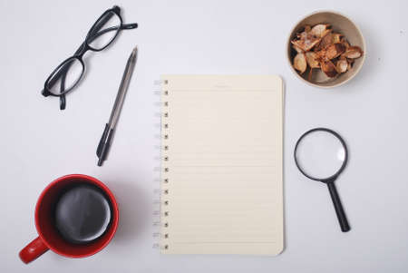 Minimalist notebook on office table desk. Workspace with notebook, spectacle, pen, magnifying glass, cup of coffee, potpourri on white background. Flat lay, top viewの写真素材
