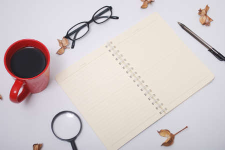 Minimalist notebook on office table desk. Workspace with notebook, spectacle, pen, magnifying glass, cup of coffee, potpourri on white background. Flat lay, top viewの写真素材