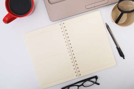 Stylish office table desk. Workspace with laptop, notebook, spectacle, pen, magnifying glass, cup of coffee on white background. Flat lay, top viewの写真素材