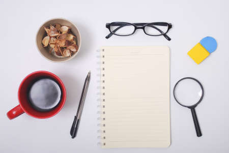 Minimalist notebook on office table desk. Workspace with notebook, spectacle, pen, magnifying glass, cup of coffee, potpourri on white background. Flat lay, top viewの写真素材