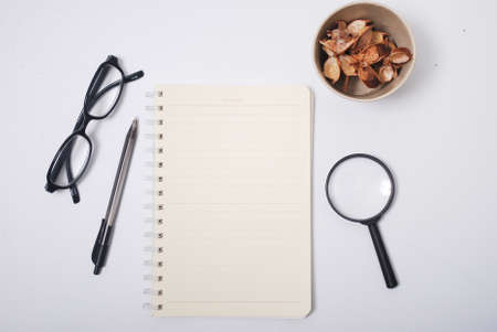 Minimalist notebook on office table desk. Workspace with notebook, spectacle, pen, magnifying glass, cup of coffee, potpourri on white background. Flat lay, top viewの写真素材
