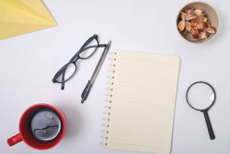 Minimalist notebook on office table desk. Workspace with notebook, spectacle, pen, magnifying glass, cup of coffee, potpourri on white background. Flat lay, top viewの写真素材