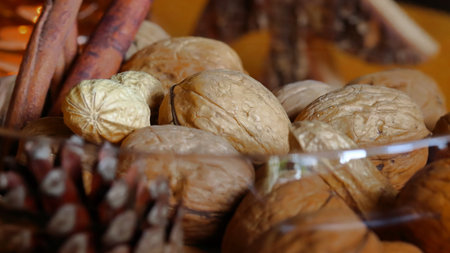Several walnuts lie with a pine cone, a peanut and cinnamon sticks in a brown glass bowl, side view,...