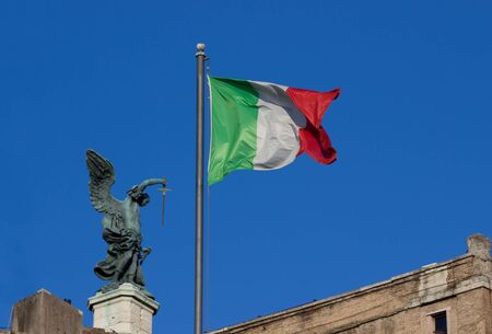 A sculpture of an angel holding a sword near an Italian Flag on the top of Castel Sant'Angelo in Rome, italyのeditorial素材