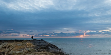 A solitary fisherman is fishing in a winter bwautiful landscape at the duskの写真素材