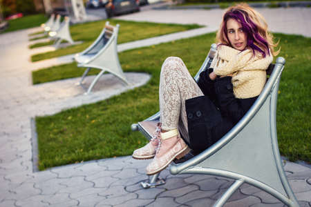 girl with colored hair coat sitting on the benchの写真素材