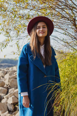 girl in hat and coat autumn walks by the riverの写真素材