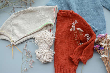 Various colors and sizes handmade baby sweaters, two items done and one in progressの写真素材
