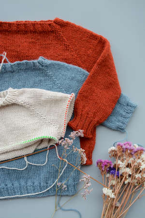 Various colors and sizes handmade baby sweaters, two items done and one in progressの写真素材