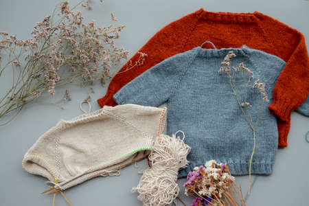 Various colors and sizes handmade baby sweaters, two items done and one in progressの写真素材
