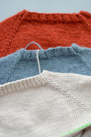 Various colors and sizes handmade baby sweaters, two items done and one in progressの写真素材