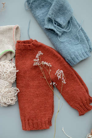 Various colors and sizes handmade baby sweaters, two items done and one in progressの写真素材