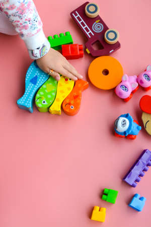 Child is playing with colorful wooden and plastic toys, on pink backgroundの写真素材