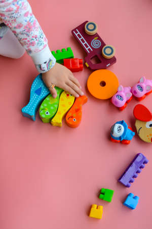 Child is playing with colorful wooden and plastic toys, on pink backgroundの写真素材