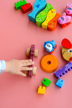 Child is playing with colorful wooden and plastic toys, on pink backgroundの写真素材